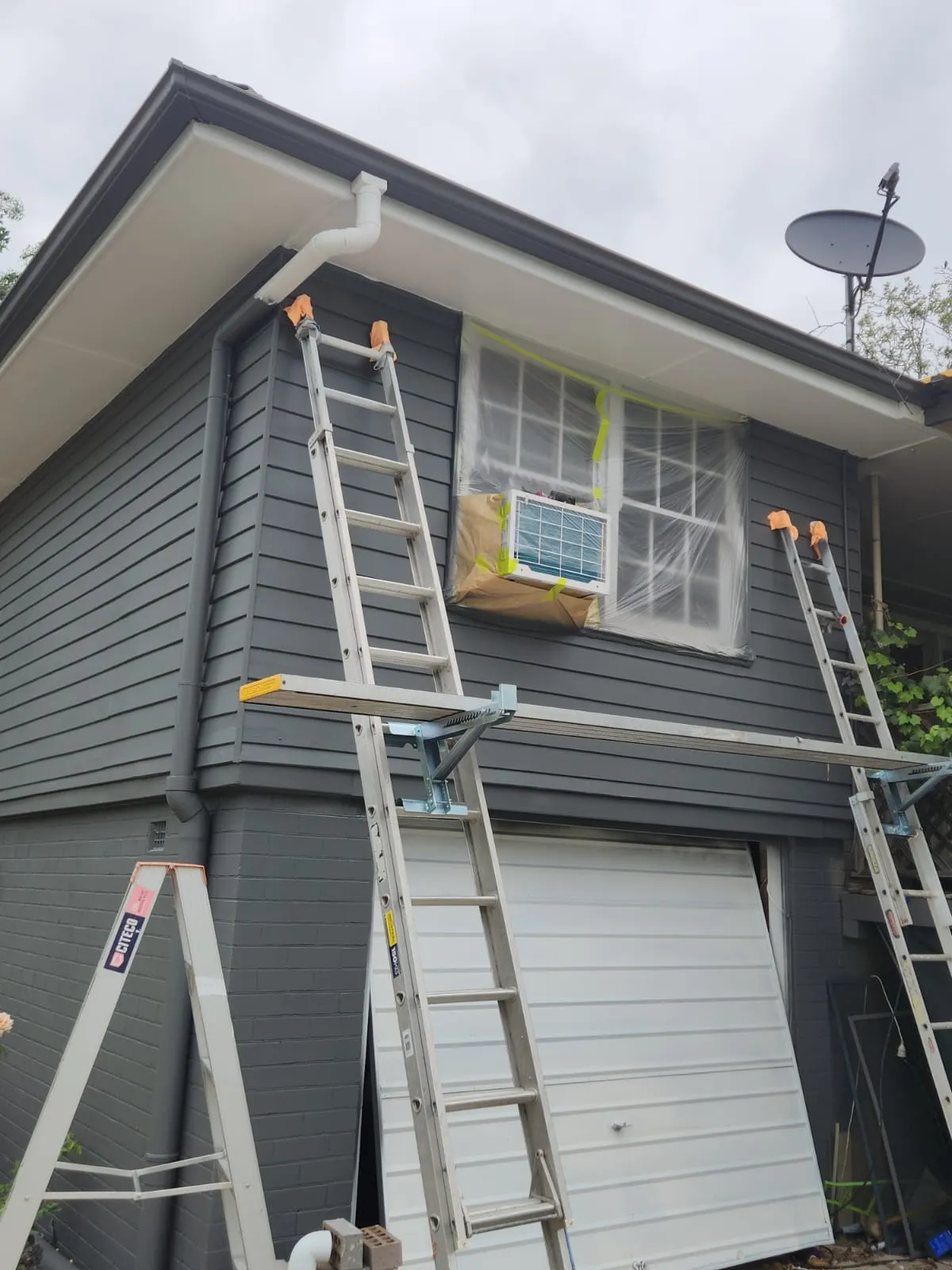 Ladders and planks set up against a dark grey Newcastle home during an exterior repaint