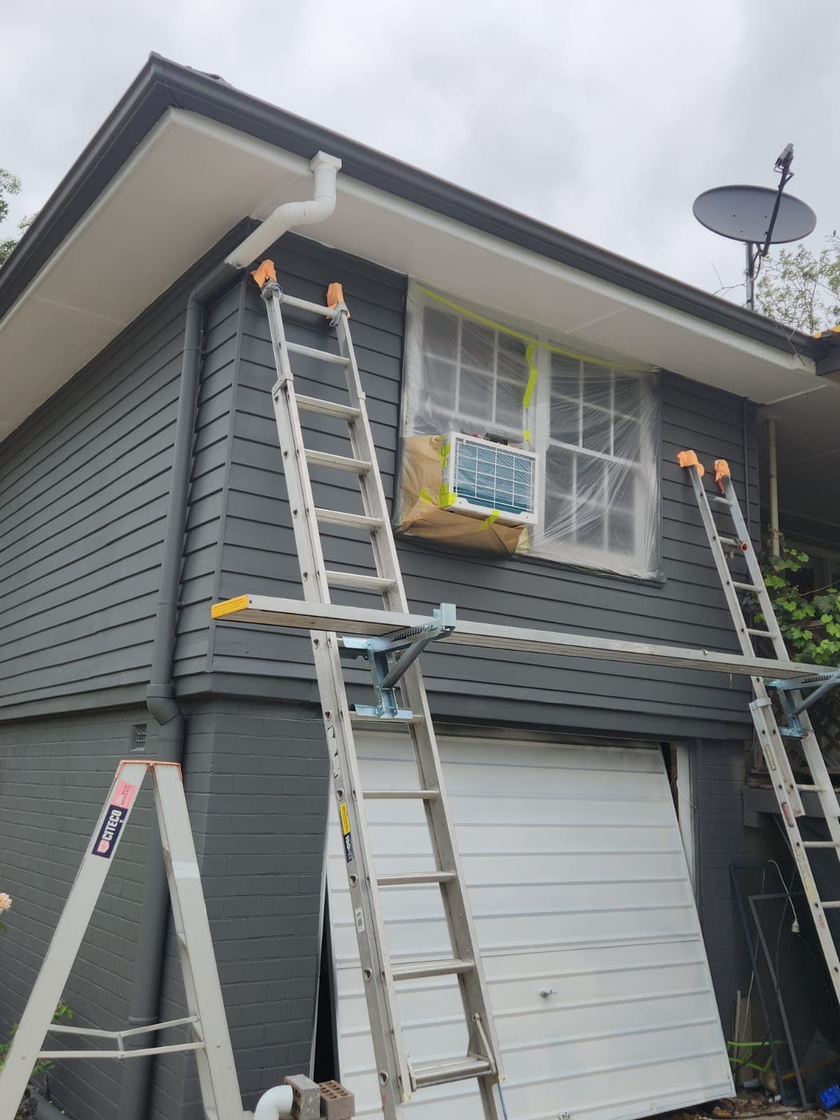Ladders and planks set up against a dark grey Kotara home during an exterior repaint