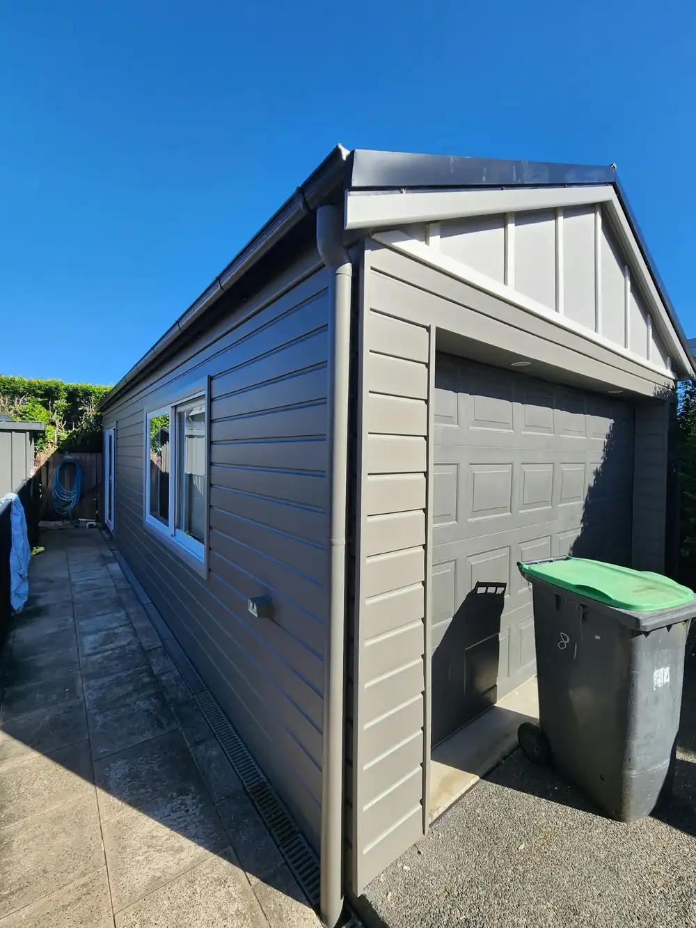 Garage side wall freshly painted grey, with white window frames and a white board-and-batten gable